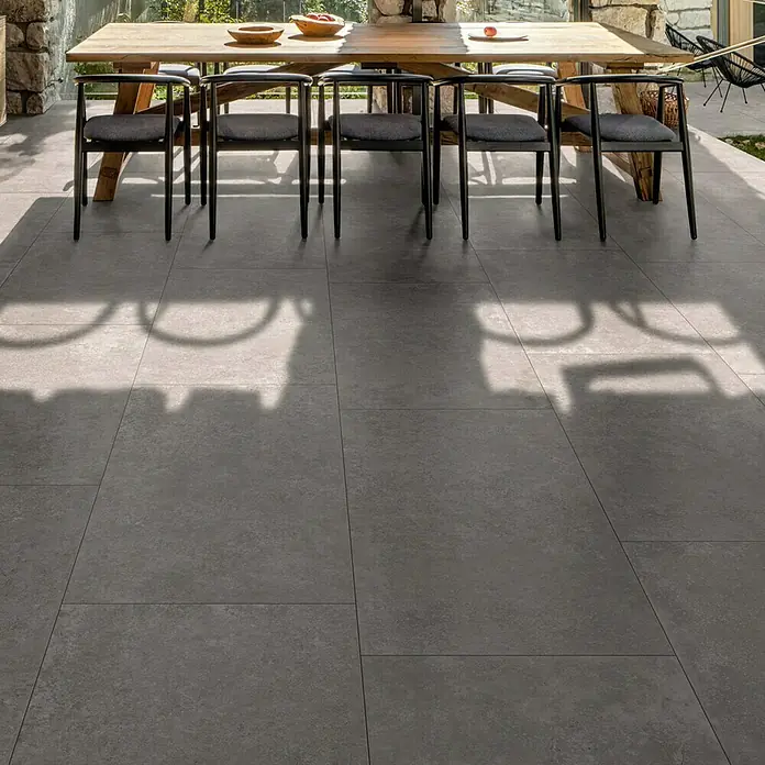 Feinsteinzeugfliese Cortina - 60 x 120 cm, Anthrazit, Matt - Großformatige graue Outdoor-Fliesen als Terrassenboden in einem Essbereich unter einem Holztisch.