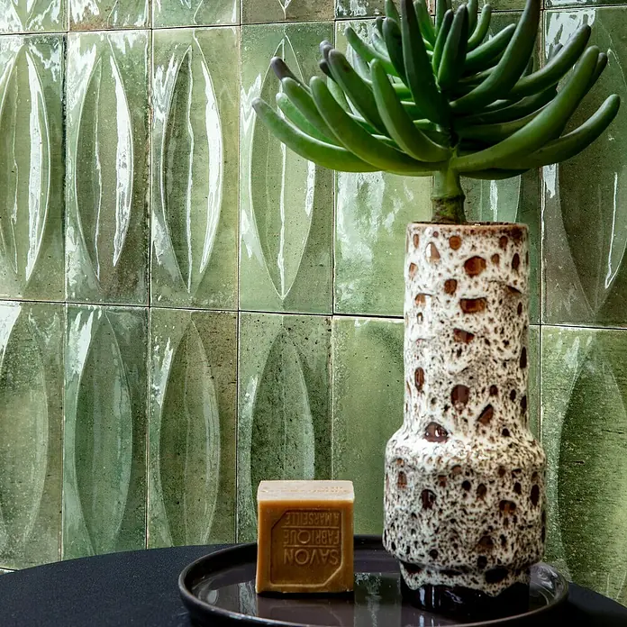 Wandfliese Stella Glossy - 7,5 x 20 cm, Giada, Glänzend - Ein hellbraunes Stück Savon de Marseille Seife auf einem dunklen Tablett, neben einer gesprenkelten Keramikvase mit einer grünen Sukkulente.