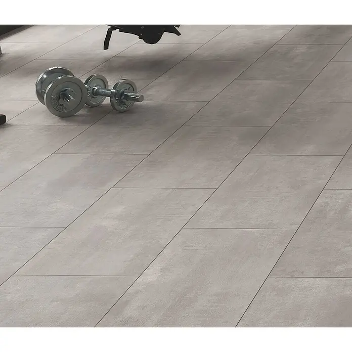 Laminat - Oxyd, Fliese, 1.288 x 330 x 8 mm - Hellgraue Betonoptik-Bodenfliesen mit rechteckigem Muster in einem Fitnessstudio, im Vordergrund Hanteln.