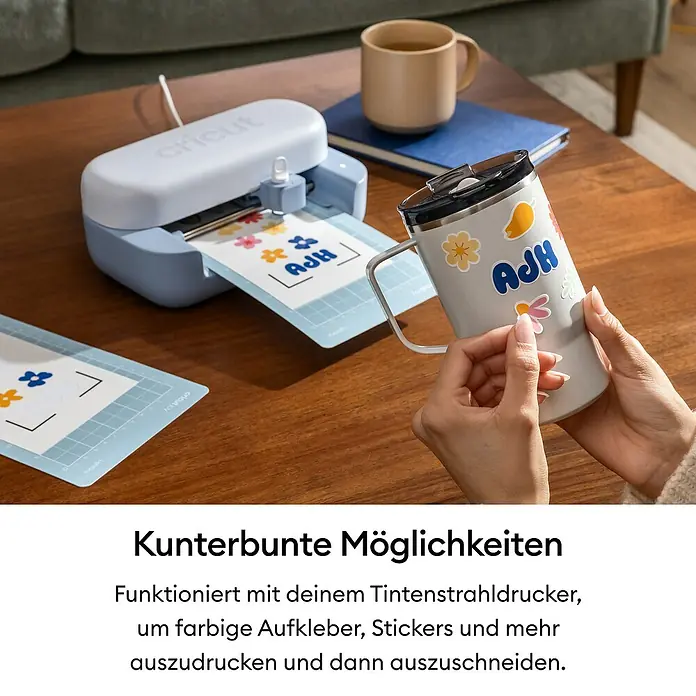 Cricut Joy Schneideplotter-Set Joy 2 Essentials Bundle - Schnittbreite: 11,4 cm, Schnittlänge: 1,2 m - Eine hellblaue und weiße Cricut-Schneidemaschine erstellt bunte Aufkleber. Eine Hand klebt einen Aufkleber auf einen silbernen Becher.