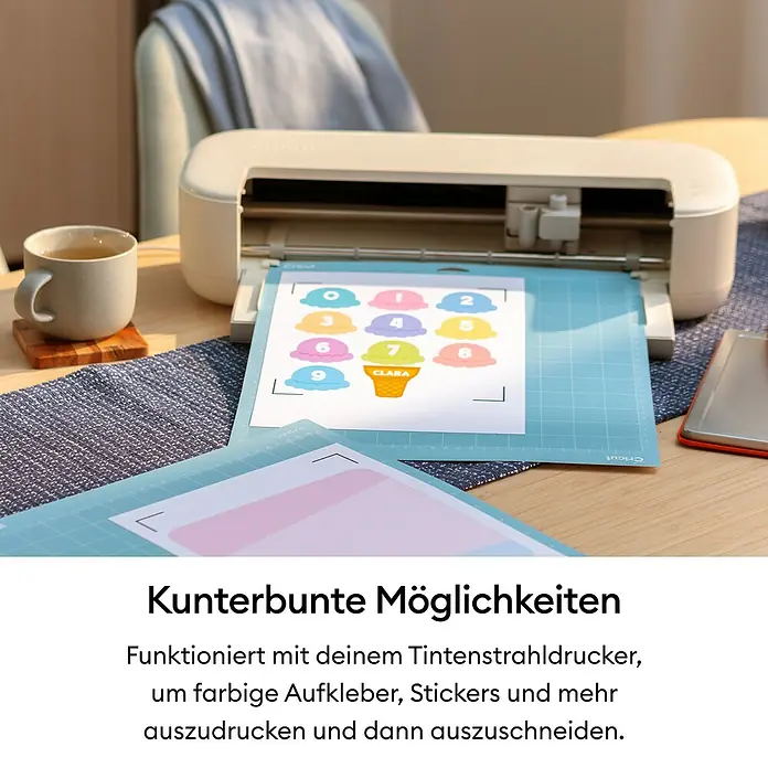 Cricut Schneideplotter-Set Explore 5 Essentials Bundle - Schnittbreite: 30,5 cm, Schnittlänge: 3,6 m - Eine weiße Schneidemaschine verarbeitet einen Bogen bunter, gedruckter Eiskugel-Aufkleber auf einer blauen Schneidematte.