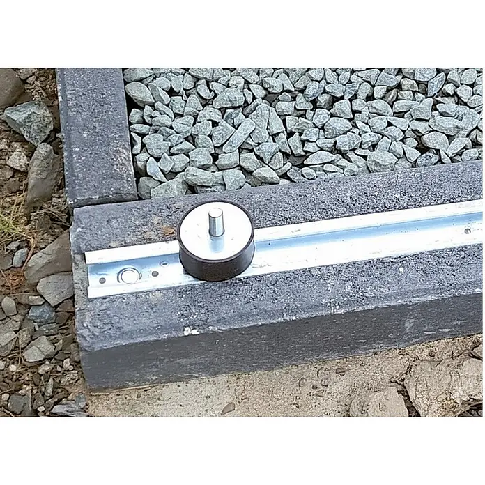 Christoph Fundamentstein Energy - 100 x 11 x 17 cm, Beton, Anthrazit - Runder dunkelbraun-silberner Endanschlag mit Stift auf einer Metallschiene in einem grauen Betonrand.
