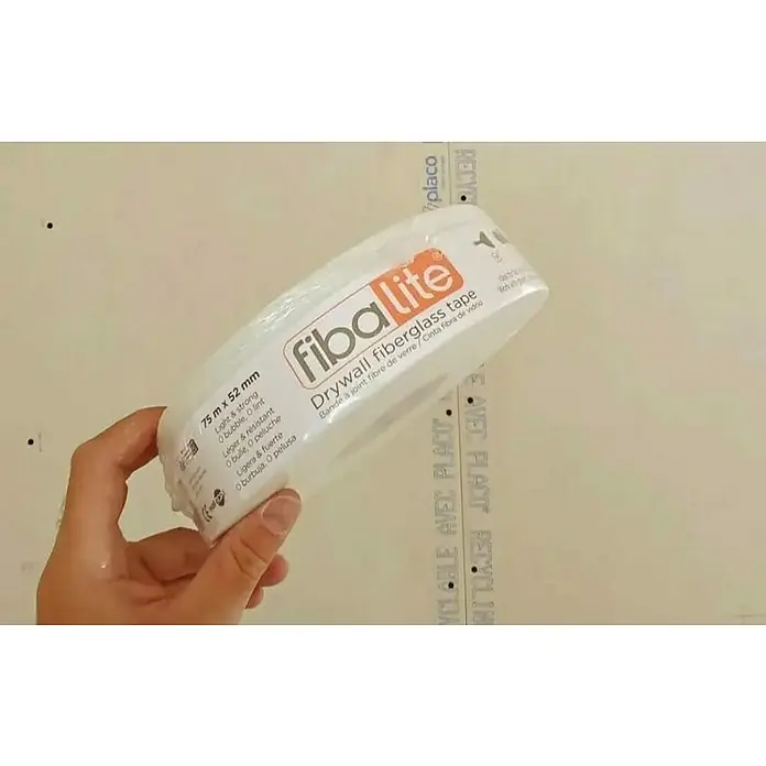 Cinta para sellado de juntas Fibalite - Largo: 75 m, Blanco - Mano sosteniendo un rollo de cinta de fibra de vidrio blanca fibalite para paneles de yeso (75m x 52mm) sobre un panel claro.
