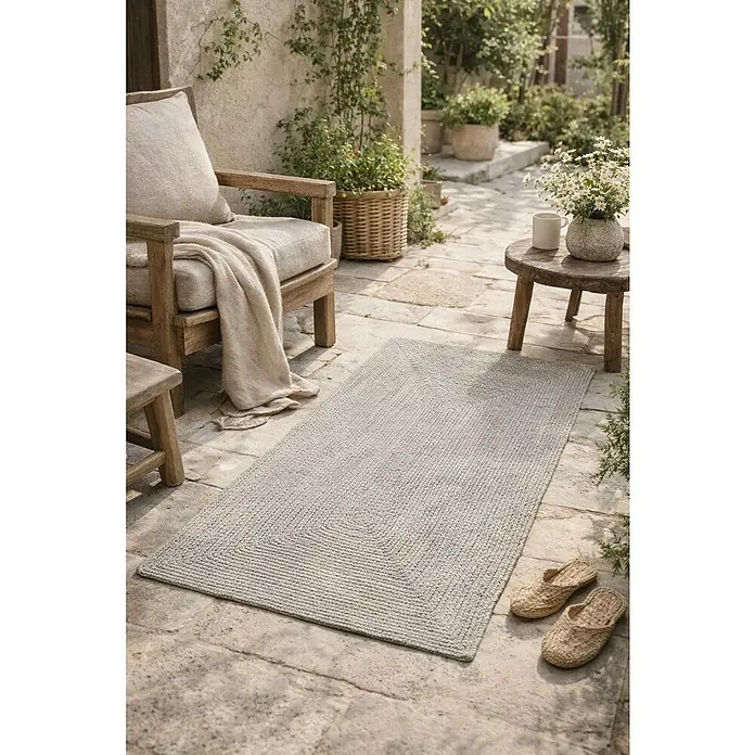 Alfombra exterior In/Out Ebro - Plata, 110 x 60 cm, 100% Polietileno - Alfombra rectangular trenzada gris sobre un patio de piedra.