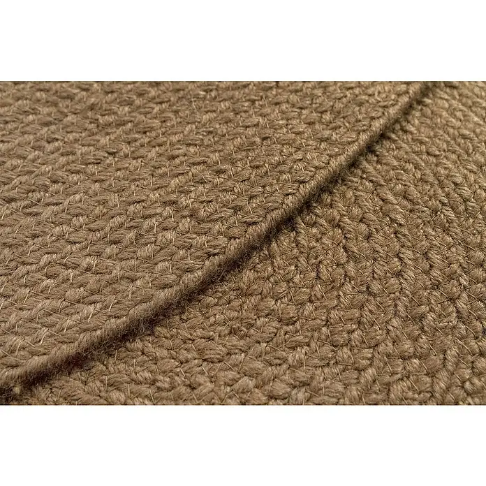 Alfombra exterior In/Out Ebro - Marrón, Diámetro: 120 cm, 100% Polietileno - Alfombra trenzada marrón con un pliegue, mostrando su fibra natural texturizada y densamente tejida.