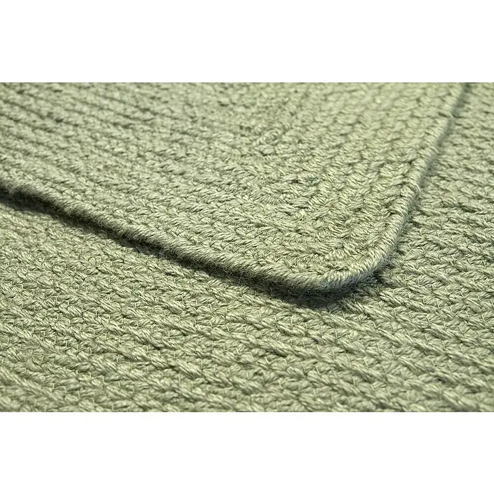Alfombra exterior In/Out Ebro - Verde, 110 x 60 cm, 100% Polietileno - Alfombra trenzada verde claro con textura tejida visible y una esquina doblada.