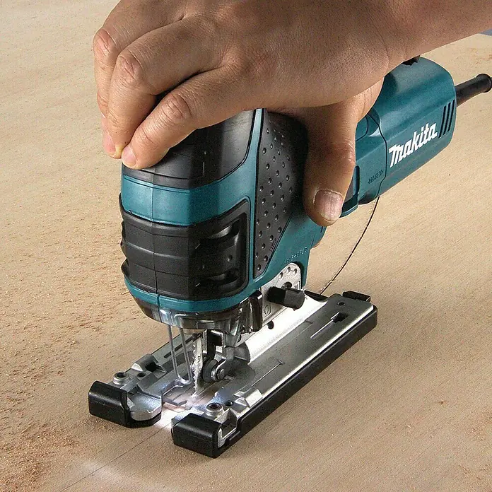 Makita Elektro-Pendelhubstichsäge 4351FCTJ - 800 /min - 2.800 /min, Max. Schnitttiefe in Holz: 135 mm, Anzahl Pendelhubstufen: 4 Stk. - Eine tealfarbene und schwarze Makita Stichsäge wird von einer Hand gehalten und schneidet eine Linie in helles Holz, umgeben von Sägespänen.