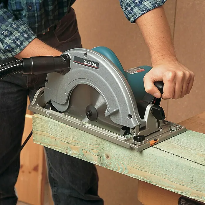 Makita Handkreissäge 5903R - 2.000 W, Durchmesser Sägeblatt: 235 mm - Eine Person sägt mit einer Makita Kreissäge mit silbernem Gehäuse und türkisfarbenem Motor hellgrünes Holz.