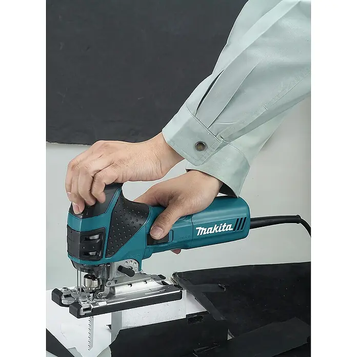 Makita Elektro-Pendelhubstichsäge 4351FCTJ - 800 /min - 2.800 /min, Max. Schnitttiefe in Holz: 135 mm, Anzahl Pendelhubstufen: 4 Stk. - Türkis und schwarze Makita Stichsäge, von Händen gehalten, schneidet dunkles Material.
