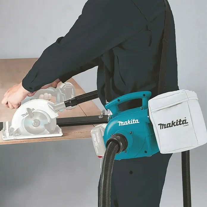 Makita LXT 18V Akku-Staubsauger DVC350Z -  - Tragbares Makita Absauggerät mit weißem Staubbeutel und schwarzem Schlauch, über der Schulter getragen, an Akku-Kreissäge beim Holzschnitt angeschlossen.