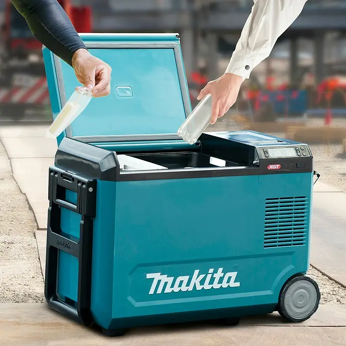 Makita Akku-Kühlbox zum Kühlen & Warmhalten CW004GZ - 18 V, Ohne Akku, 29 l - Ein türkisfarbener Makita Kühl-/Gefrierbox mit geöffnetem Deckel, der auf einer Baustelle mit Getränk und Snack befüllt wird. Er hat schwarze Akzente und Räder.