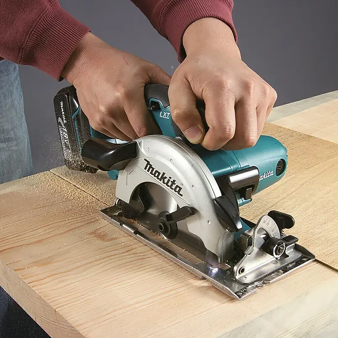Makita LXT 18V Akku-Handkreissäge DSS501RTJ - 18 V, 2 Akkus, 5 Ah, 0 U/min - 3.600 U/min - Akku-Kreissäge Makita LXT 18V, türkis/silber, schneidet helles Holz, von Händen geführt.