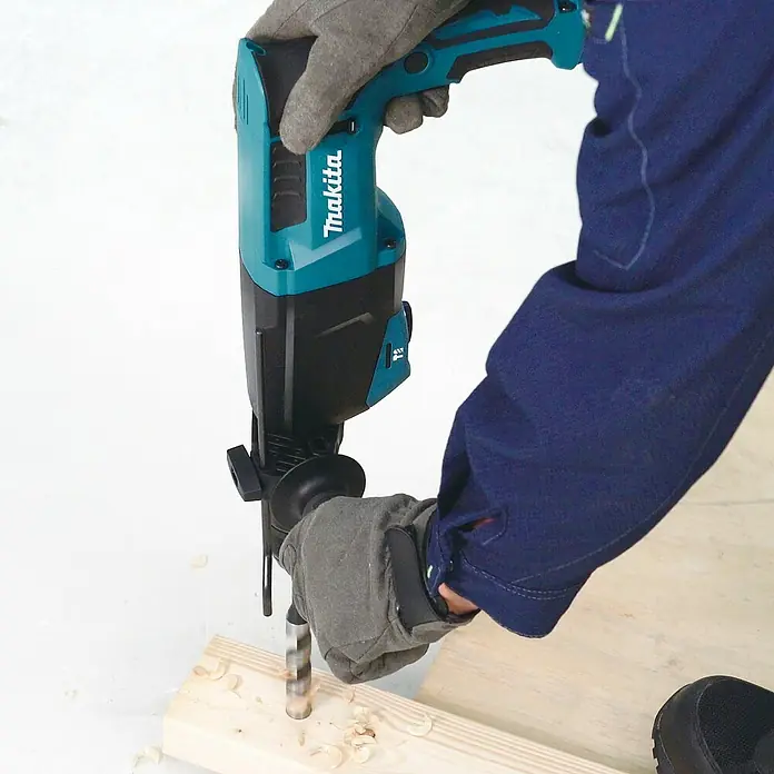 Makita Kombihammer HR2670FTX1 - 800 W, 3 J, SDS-Plus-Aufnahme - Türkis-schwarzer Makita Bohrhammer, von einer behandschuhten Hand gehalten, bohrt aktiv in ein Holzbrett, wobei Holzspäne entstehen.