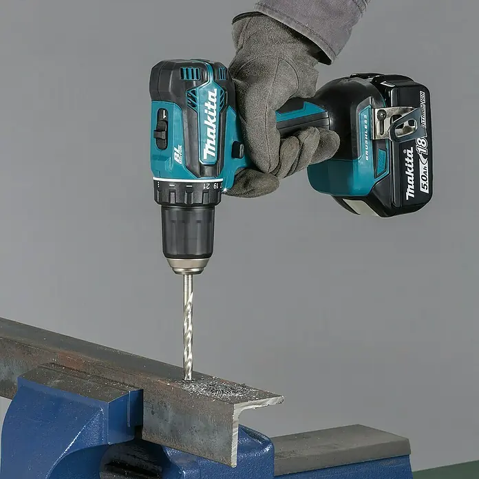 Makita LXT 18V Akku-Bohrschrauber-Set DDF485RFJ - 18 V, 2 Akkus, 50 Nm - Eine behandschuhte Hand bedient einen Makita Akku-Bohrschrauber, der in ein Metallprofil bohrt, das in einem Schraubstock eingespannt ist. Metallspäne sind sichtbar.