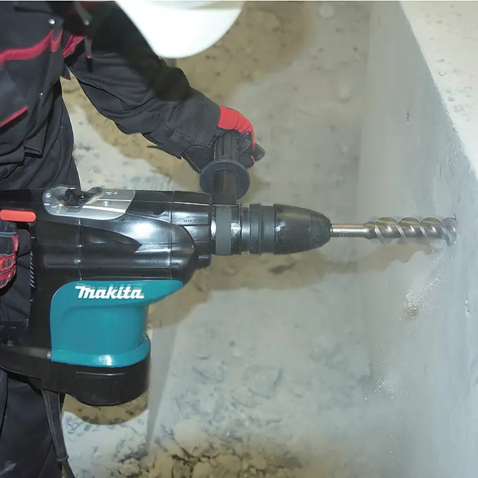 Makita Kombihammer HR4510C - 1.350 W, 9,4 J, SDS-Max-Aufnahme - Schwarzer und türkisfarbener Makita Bohrhammer bohrt aktiv ein Loch in eine Betonwand.