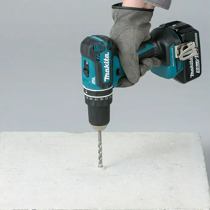 Makita LXT 18V Akku-Schlagschrauber DHP485Z - 18 V, Ohne Akku, 50 Nm - Eine behandschuhte Hand hält eine türkis-schwarze Makita-Bohrmaschine mit bürstenlosem Motor und 5.0Ah Akku, die in eine helle Platte bohrt.