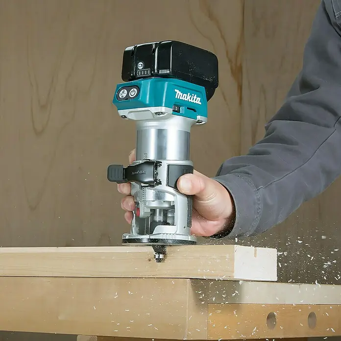 Makita LXT 18V Akku-Multifunktionsfräse DRT50ZJX2 - 18 V, Ohne Akku, Leerlaufdrehzahl: 10.000 U/min - 30.000 U/min - Eine Person bedient einen türkis-silbernen Makita Akku-Fräser und bearbeitet Holz. Holzspäne fliegen um das Werkzeug.