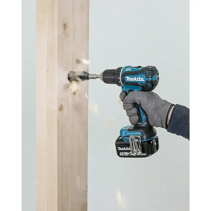 Makita LXT 18V Akku-Bohrschrauber-Set DDF485RFJ - 18 V, 2 Akkus, 50 Nm - Eine behandschuhte Hand hält einen blau-schwarzen Makita Akku-Bohrschrauber, der aktiv in einen hellen Holzbalken bohrt und Holzspäne erzeugt.
