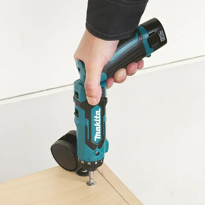 Makita Akkuschrauber DF012DSE - 7,2 V, 2 Akkus, 1,5 Ah - Eine Hand verwendet einen blau-schwarzen Makita Akkuschrauber, um eine schwarze Lenkrolle an einer hellen Holzoberfläche zu befestigen.