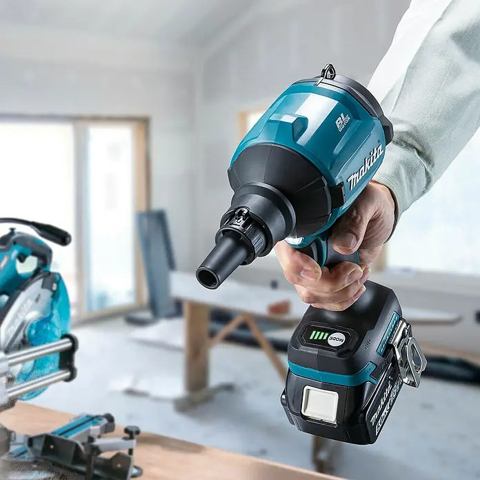 Makita LXT 18V Akku-Gebläse DAS180Z - 18 V, Ohne Akku, 200 mm/s - Hand hält einen türkisen und schwarzen Makita Trockenbauschrauber mit Akku in einer Bauumgebung.