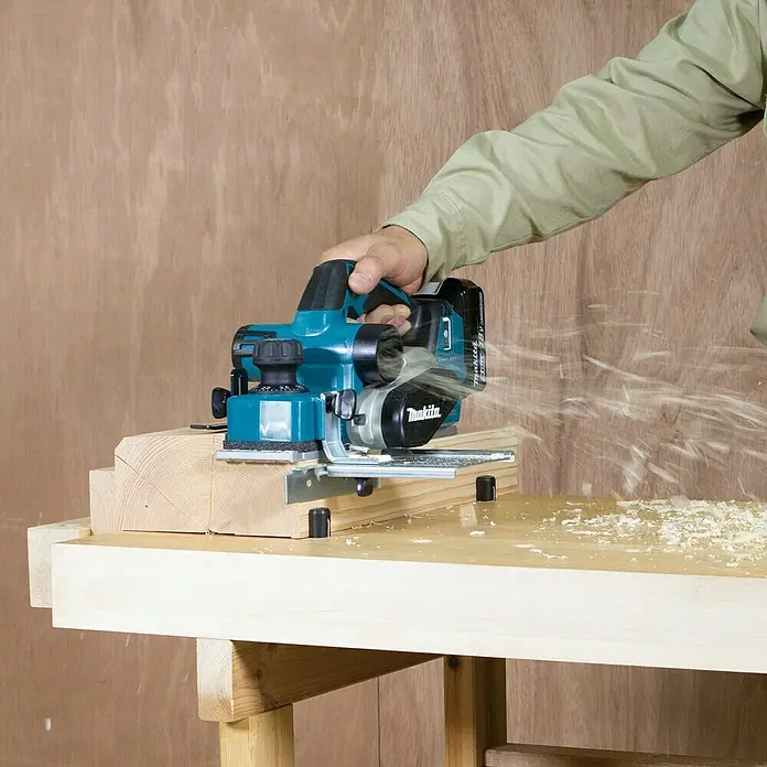 Makita LXT 18V Akku-Hobel - 18 V, Ohne Akku, Leerlaufdrehzahl: 12.000 U/min - Eine Person benutzt einen blauen Makita Akku-Hobel, um ein Holzbrett zu glätten, wobei Späne entstehen.