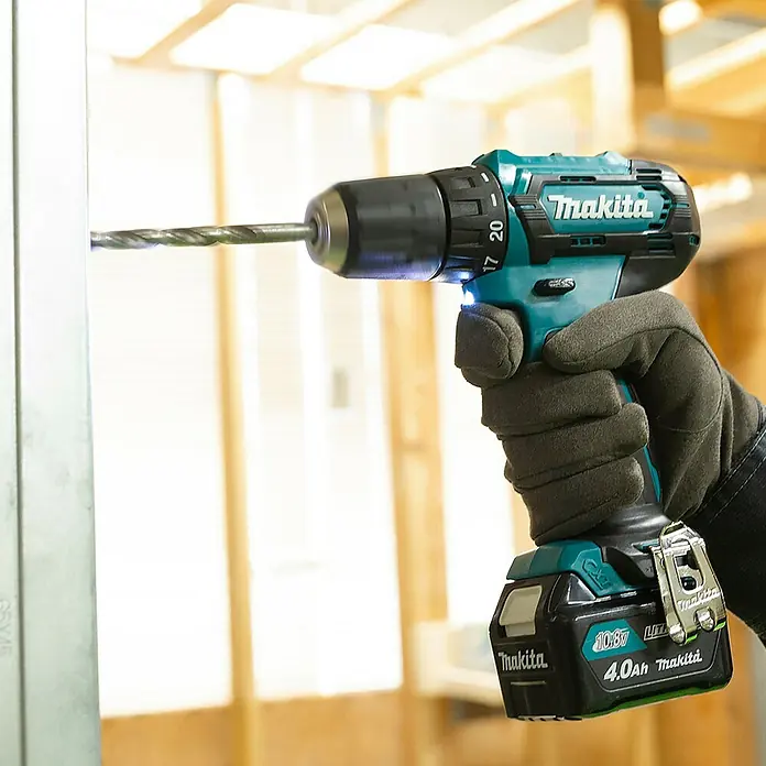 Makita CXT 12V max. Akku-Bohrschrauber DF333DZ - 12 V, Ohne Akku - Eine behandschuhte Hand hält eine türkis-schwarze Makita Akku-Bohrmaschine, die in ein Metallprofil bohrt.