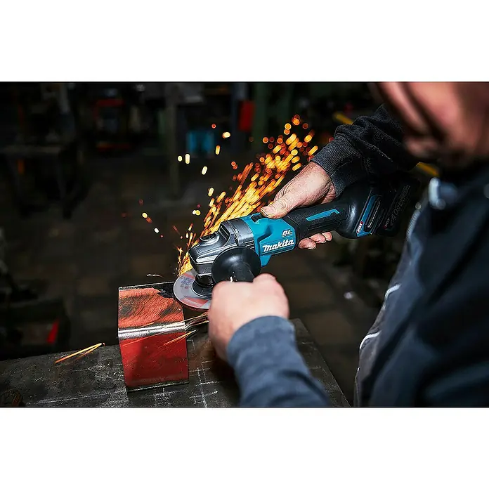 Makita XGT 40V max. Akku-Winkelschleifer GA008GM201 - 2 Akkus, 4 Ah, Durchmesser Scheibe: 125 mm - Eine Person nutzt einen türkisfarbenen und schwarzen Makita Winkelschleifer, um Metall zu schneiden, wobei helle orange Funken entstehen.