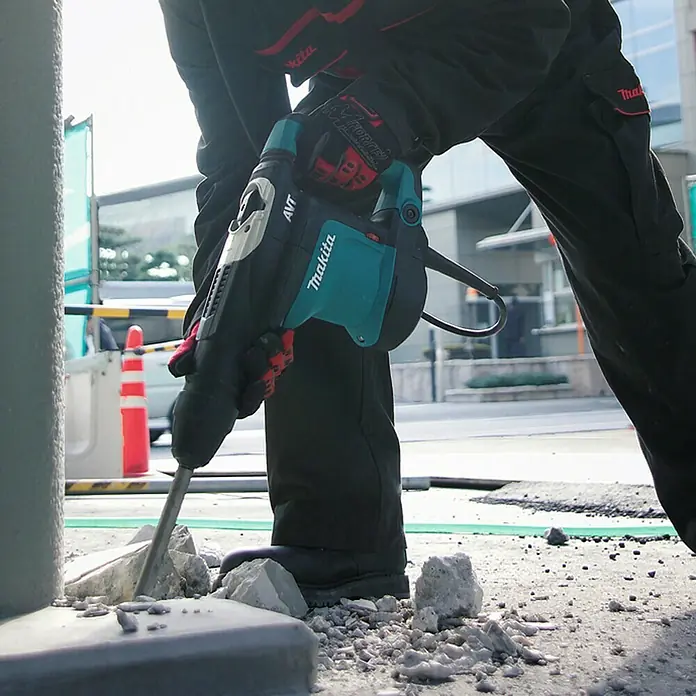 Makita Kombihammer HR3541FCX - 850 W, 5,7 J, SDS-Max-Aufnahme - Person bricht Beton mit einem türkis-schwarzen Makita Abbruchhammer auf der Straße.