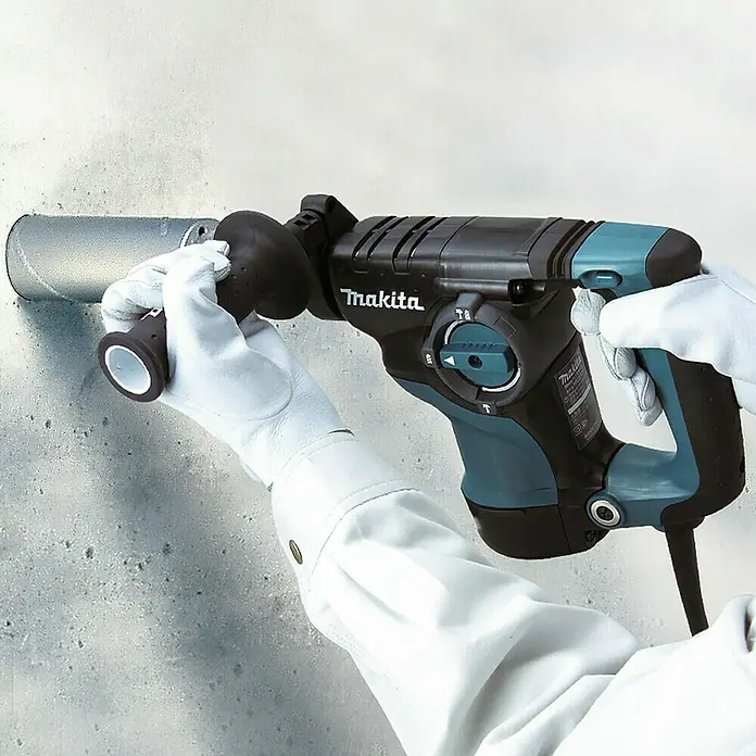 Makita Kombihammer HR2811FT - 800 W, 2,8 J, Schnellspannbohrfutter - Person in weißen Handschuhen benutzt einen schwarz-türkisen Makita Bohrhammer an einem Metallrohr in einer Betonwand.