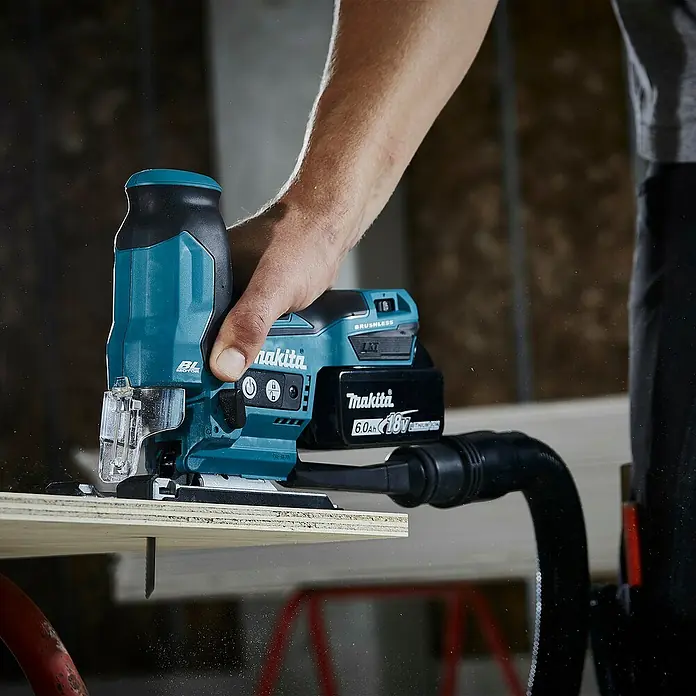 Makita LXT 18V Akku-Pendelhubstichsäge DJV185Z - 18 V, Ohne Akku, Leerlaufhubzahl: 800 /min - 3.000 /min - Eine Person verwendet eine türkise und schwarze Makita 18V Akku-Stichsäge mit Staubabsaugung, um Holz zu schneiden.