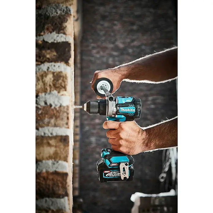 Makita XGT 40V max. Akku-Schlagbohrschrauber HP001GZ - 40 V, Ohne Akku - Hände halten einen schwarz-türkisen Makita Akkubohrer, der aktiv in eine Ziegelwand bohrt.