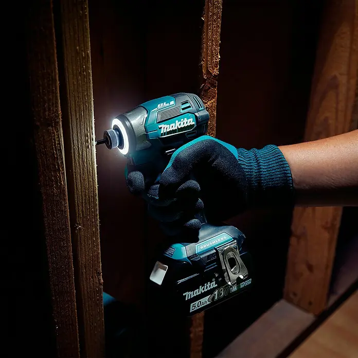 Makita LXT 18V Akku-Schlagschrauber DTD173Z - 18 V, Ohne Akku - Türkis-schwarzer Makita Schlagschrauber, von einer behandschuhten Hand gehalten, beleuchtet einen Holzständer im Dunkeln.