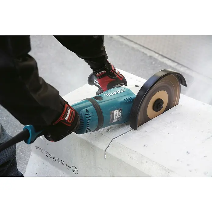 Makita Elektro-Winkelschleifer GA9040RF01 - 2.600 W, Durchmesser Scheibe: 230 mm, Leerlaufdrehzahl: 0 U/min - 6.600 U/min - Eine Person schneidet mit einem türkisblauen Makita Winkelschleifer und rotierender Klinge einen Betonblock, trägt Arbeitshandschuhe.