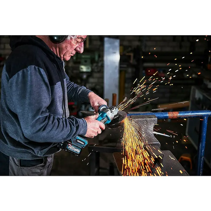 Makita XGT 40V max. Akku-Winkelschleifer GA008GM201 - 2 Akkus, 4 Ah, Durchmesser Scheibe: 125 mm - Mann in Schutzkleidung nutzt einen hellblauen/schwarzen Akku-Winkelschleifer zum Trennen eines Metallrohrs, dabei entstehen helle Funken.