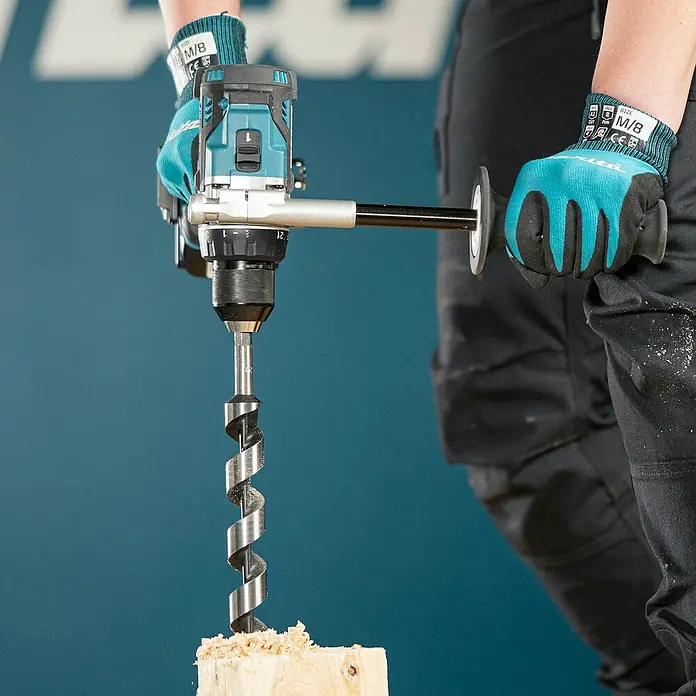 Makita LXT 18V Akku-Bohrschrauber DDF492RTJ - 18 V, 2 Akkus, 130 Nm - Person in blau-schwarzen Handschuhen bedient blau-schwarze Bohrmaschine mit großem Holzbohrer zum Bohren in Holz, Späne fallen.