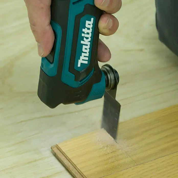 Makita CXT 12V max. Akku-Multifunktionswerkzeug TM30DZ - 12 V, Ohne Akku - Hand bedient ein türkisfarbenes und schwarzes Makita-Oszillierwerkzeug, das in ein helles Holzbrett schneidet und feinen Sägemehl erzeugt.