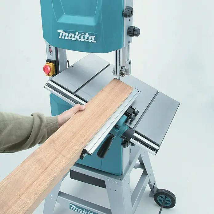 Makita Bandsäge LB1200F - 900 W, Durchlasshöhe: 165 mm, Durchlassbreite: 305 mm - Blaue Makita Bandsäge schneidet ein Holzbrett, von einer Hand geführt. Grauer Tisch und Rahmen.