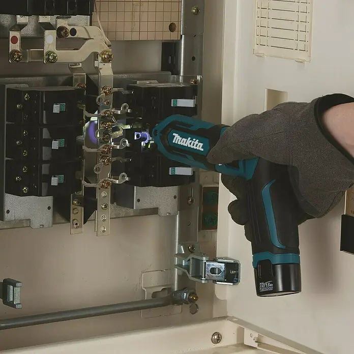 Makita Akku-Schlagschrauber TD022DSE - 7,2 V, 2 Akkus, 1,5 Ah - Behandschuhte Hand nutzt teal-schwarzen Makita Akku-Schrauber an Schalttafel.