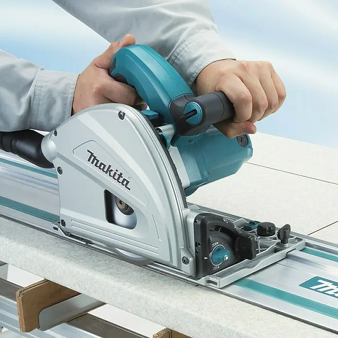 Makita Tauchsäge SP6000J1 mit Makpac und Führungsschiene - 1.300 W, 6.400 U/min - Person bedient eine silberne und türkise Makita Tauchsäge mit Führungsschiene, um eine helle Platte zu schneiden.