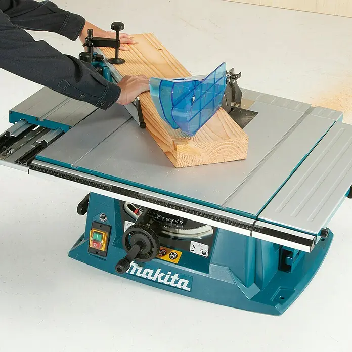 Makita Tischkreissäge MLT100NX1 mit Untergestell - 1.500 W, Durchmesser Sägeblatt: 260 mm, Schnitttiefe bei 90 °: 93 mm - Türkise Makita Tischsäge mit silberner Platte, von einer Person zum Schneiden eines Holzbretts verwendet, mit blauem Sägeblattschutz.