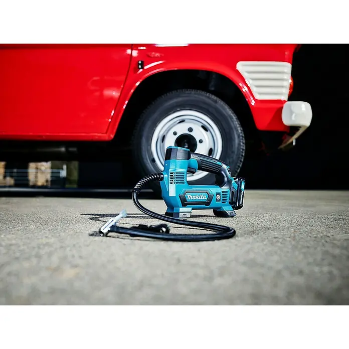 Makita CXT 12V max. Akku-Kompressor MP100DZ - 12 V, Li-Ionen, Ohne Akku, Max. Druck: 8,3 bar - Türkiser und schwarzer Makita Reifenfüller mit Schlauch und Düse, auf Asphalt neben einem Autoreifen.