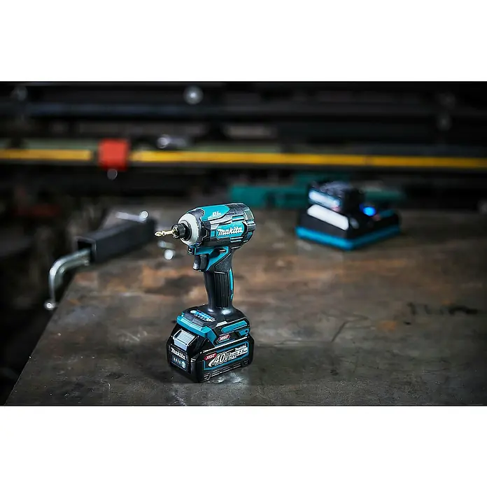 Makita XGT 40V max. Akku-Schlagschrauber TD001GD201 - 40 V, 2 Akkus, 2,5 Ah - Kabelloser, blau-schwarzer Makita Schlagschrauber mit Akku und Schrauberbit auf einem Werkstatttisch neben einem verschwommenen Ladegerät.