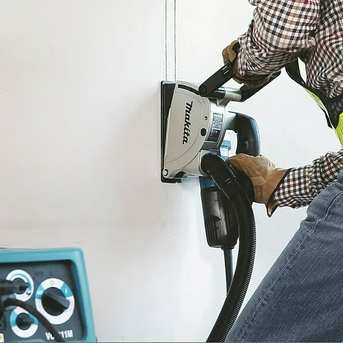 Makita Mauernutfräse SG1251J - 1.400 W, Durchmesser Scheibe: 125 mm - Makita Mauerschlitzer schneidet Nuten in eine Wand, angeschlossen an einen Staubsauger.