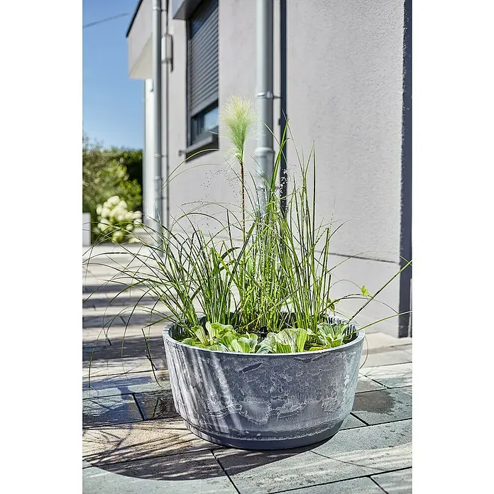 Heissner Gartenbrunnen Solar Wassergarten Aquatopia - Kunststoff, Hellgrau - Ein großer, strukturierter grauer Pflanzkübel mit Wasserpflanzen auf einer modernen Terrasse.