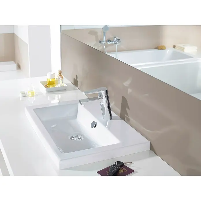 Hansa Twist Waschtischarmatur Typ 2 - Mit Zugstange, Chrom, Glänzend - Weißes Keramikwaschbecken mit modernem Chromwasserhahn auf einer Arbeitsplatte in einem hellen Badezimmer.