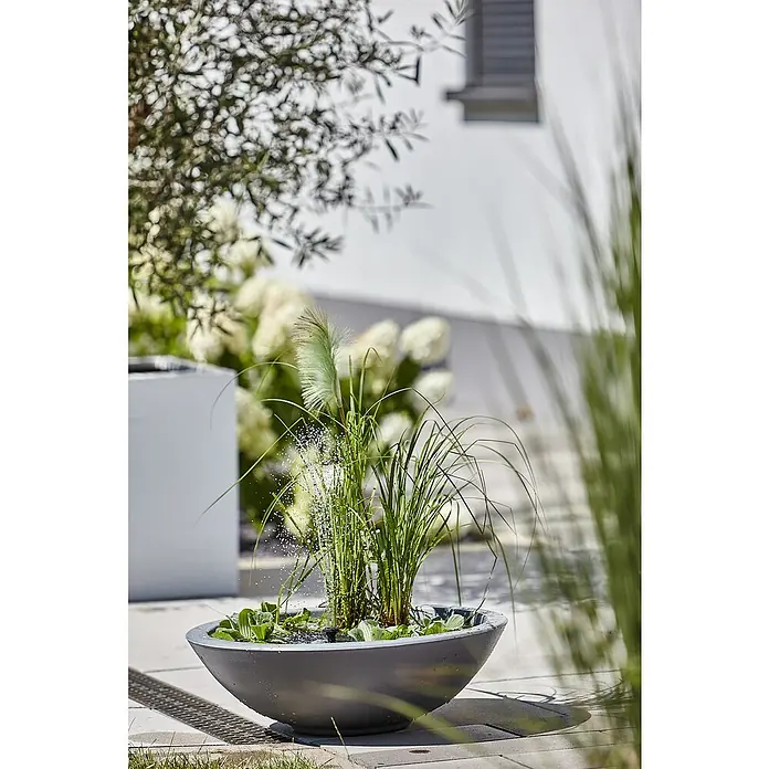 Heissner Zierbrunnen Solar Wassergarten Lotusgarden - Anthrazit, L x B x H: 58 x 58 x 19 cm - Eine moderne, graue, schalenförmige Wasserfontäne mit Wasserpflanzen auf einer gepflasterten Terrasse.
