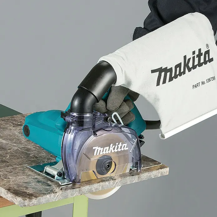 Makita Elektro-Trennschleifer 4100KB - 1.400 W, 12.200 U/min, Durchmesser Sägeblatt: 125 mm - Makita türkisfarbene Nasssäge mit transparentem Schutz und Staubfangbeutel schneidet eine gesprenkelte Granitarbeitsplatte.
