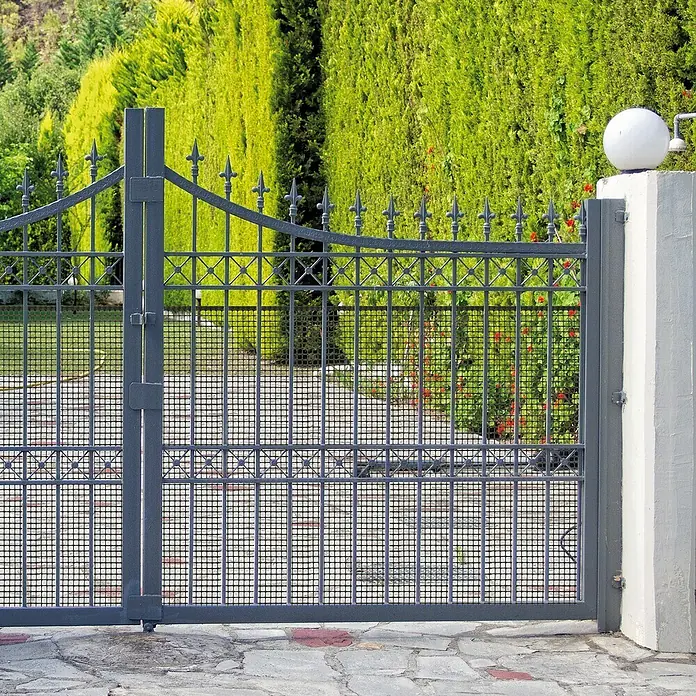 Tenax Malla protectora Quadra 10 - L x Al: 5 x 1 m, Antracita - Portón metálico gris oscuro con puntas decorativas y malla, abriendo a un camino de jardín verde.