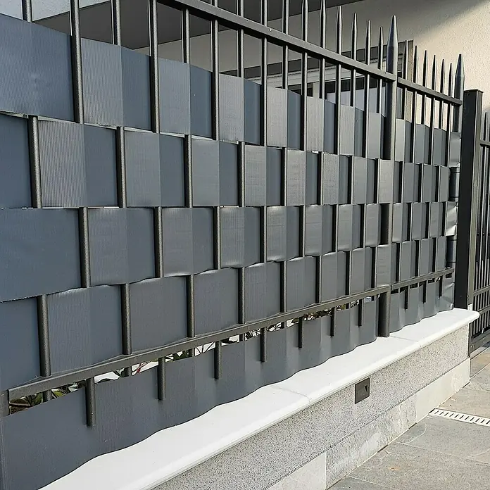 Tenax Malla de ocultación Twist - 35 x 0,19 m, Antracita - Malla de privacidad de PVC gris tejida a través de una valla metálica oscura, que ofrece privacidad semiopaca para exteriores.