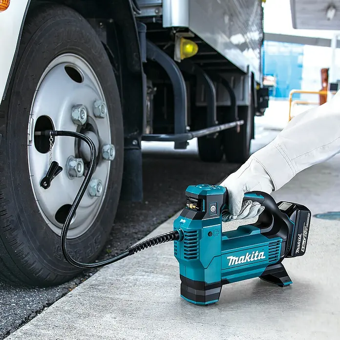 Makita LXT 18V Compresor de batería DMP181Z - 18 V, Sin batería, 11,1 bar - Inflador de aire Makita turquesa y negro, sujetado por una persona, inflando un neumático de camión grande.
